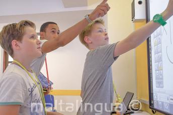 A teacher helping 2 students at an interactive whiteboard